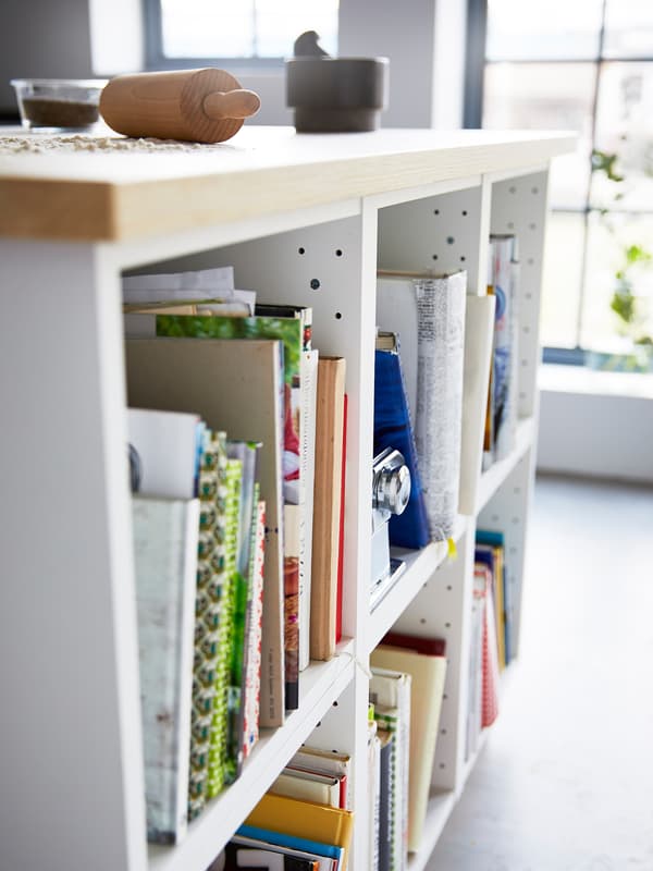 A close-up of a white kitchen island with a wooden worktop showing open cabinets storing cookbooks.