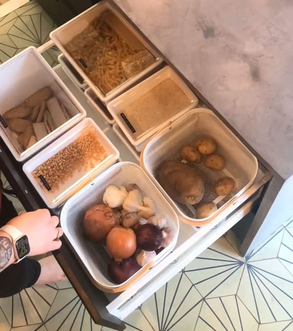 A close up of a wide kitchen drawer with storage containers for dry food such as pasta and flour.