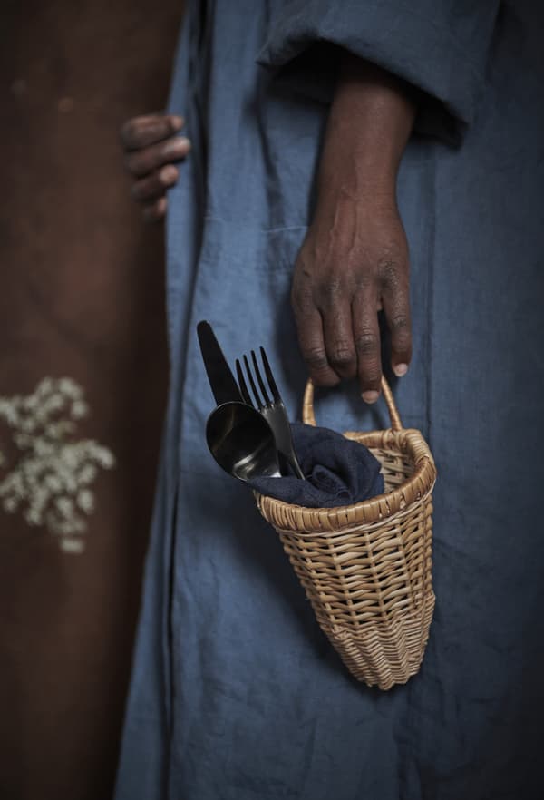 A close-up of a woman holding a small wicker basket containing cutlery.
