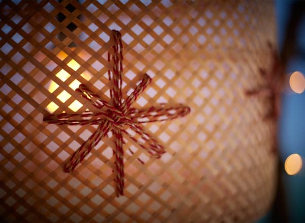 A close-up of a woven bamboo lamp decorated with paper holiday ribbon and hanging in a window.