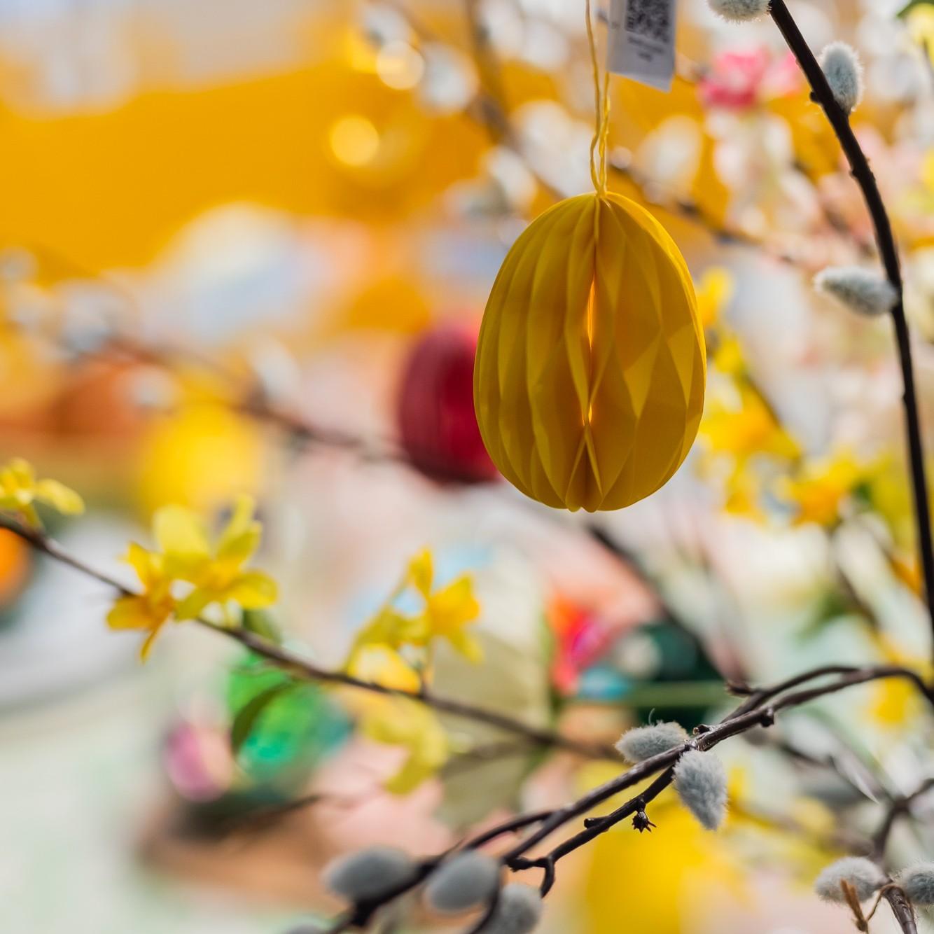 A close-up of a yellow, oval-shaped paper ornament hung in a branch. 
