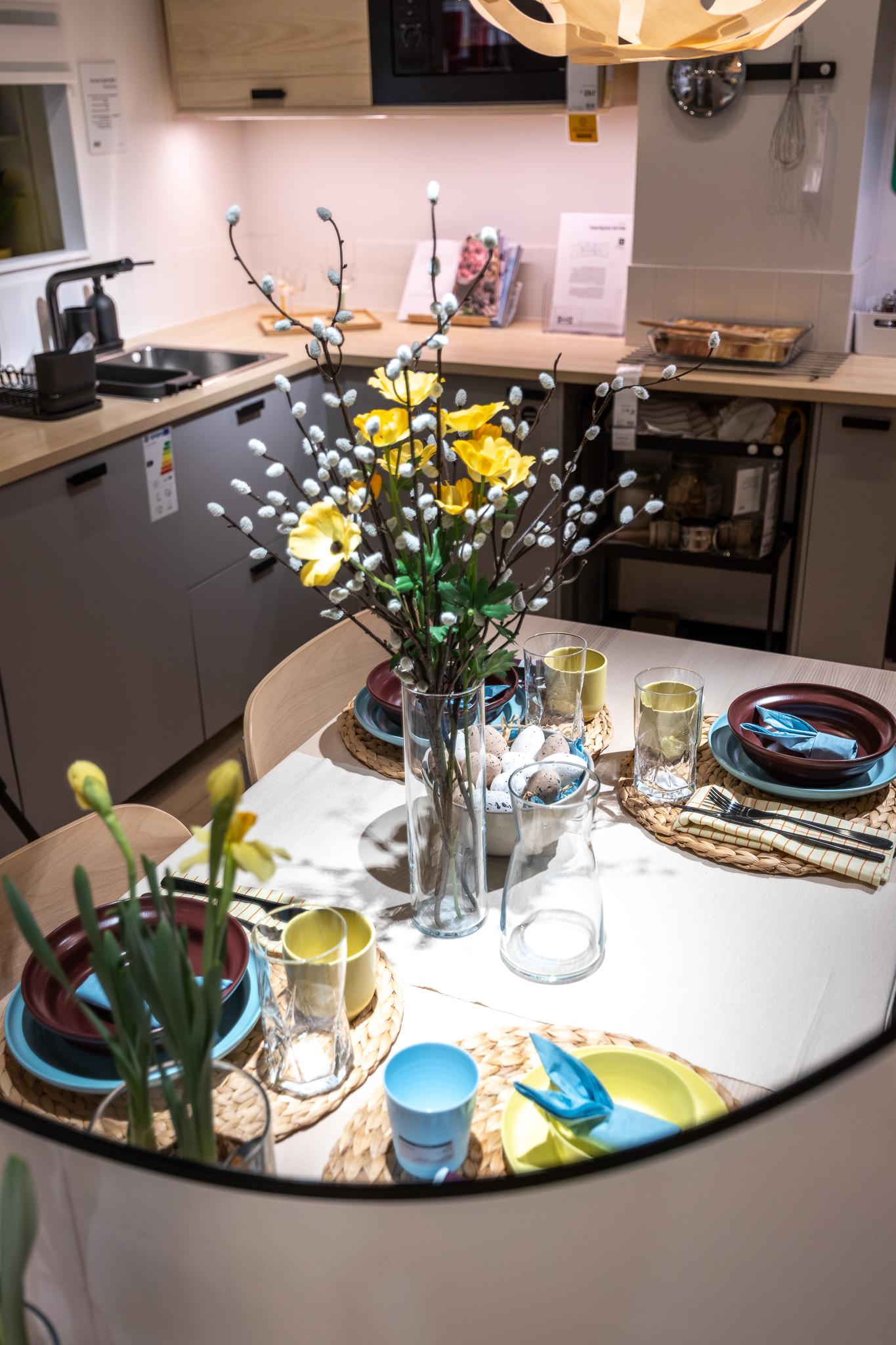 A close-up of an Easter place setting with layered tableware, a folded blue napkin, a yellow mug, and a glass.