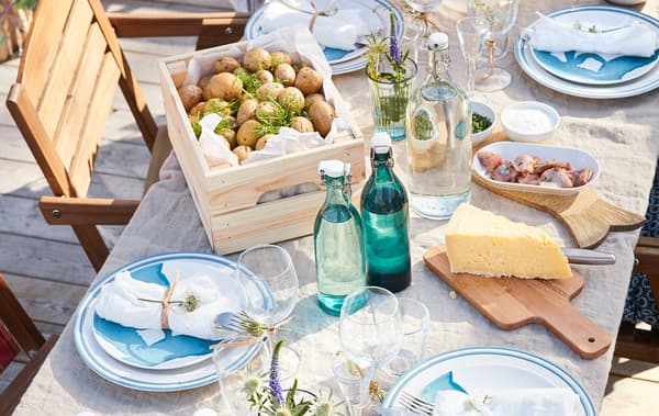 A close up of an outdoor dining table with dinnerware, glasswar, food and drink.