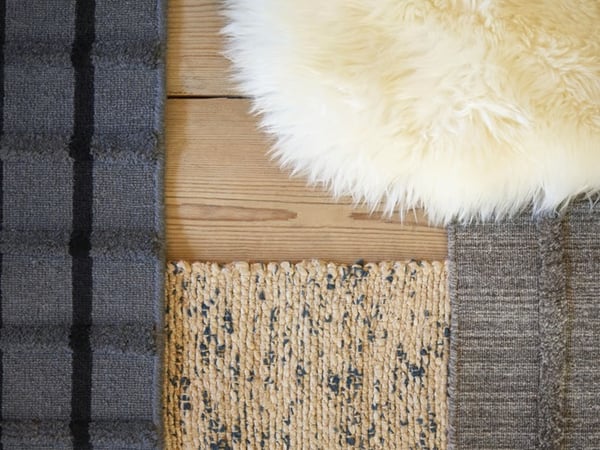 A close-up of assorted textured rugs laid out on a wooden floor.