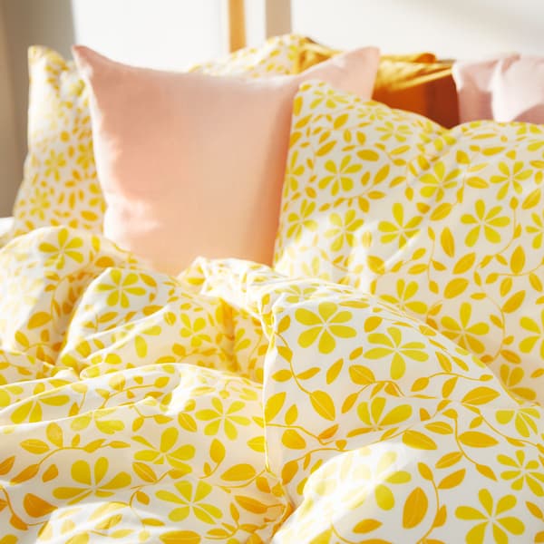 A close-up of bedding with yellow flower pattern and pale pink cushions.