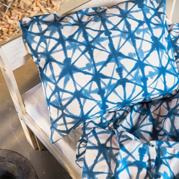 A close-up of blue patterned STJÄRNFLOCKA bedding on a bed with wooden frame.