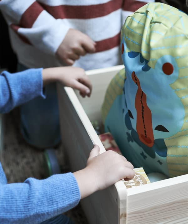 A close-up of children’s hands inside a wooden box with a soft toy inside.
