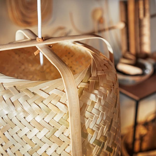 A close-up of cylindrical KNIXHULT pendant lamp shows the variations of its woven light and dark bamboo with exterior braces.