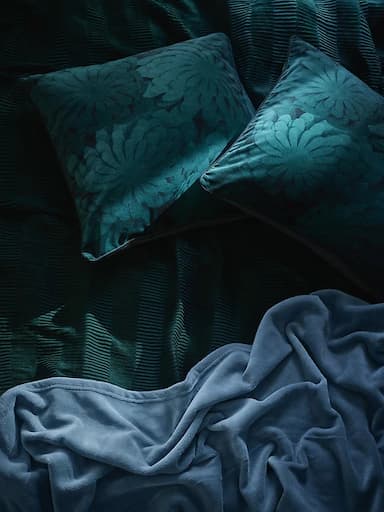 A close-up of dark green and blue bedding and cushions.
