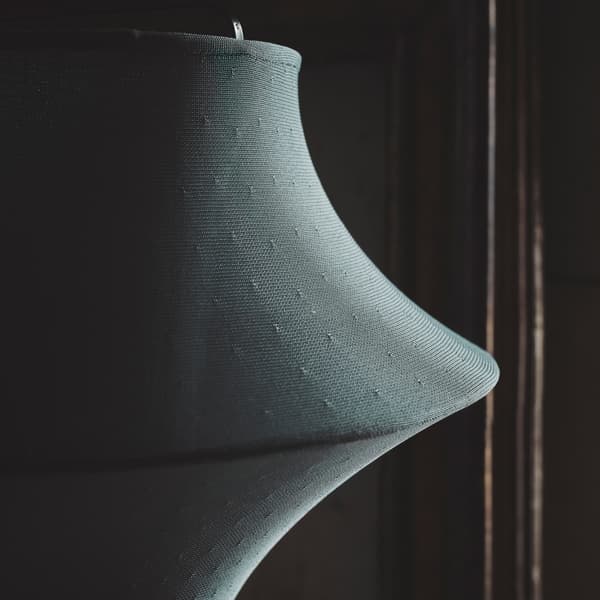 A close-up of FYXNÄS floor lamp with a double-layered textile in turquoise placed on a lamp frame with a spacey design.
