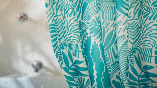 A close-up of GATKAMOMILL shower curtain with a leafy and playful pattern in turquoise and white in connection to a bathtub.