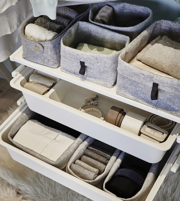 A close-up of grey RAGGISAR felt boxes with folded clothes on adjustable shelves, white plastic pull-out boxes underneath.