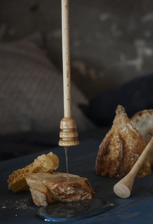 A close-up of honey drizzling from a dipper onto chunks of bread.