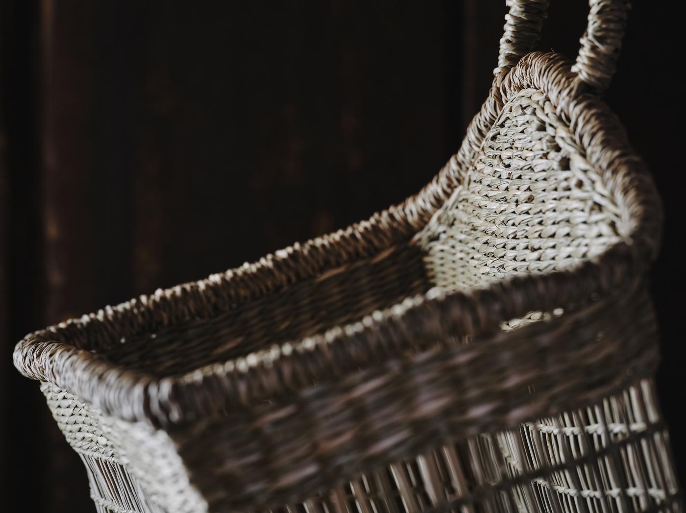A close-up of LUSTIGKURRE basket woven in natural seagrass with a handle placed in dark surroundings.