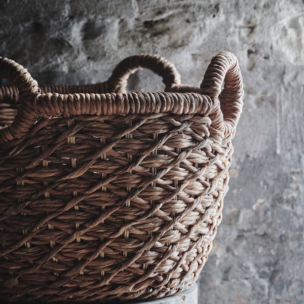 A close-up of LUSTIGKURRE basket woven in nipa palm with four round handles placed on a wooden stool.