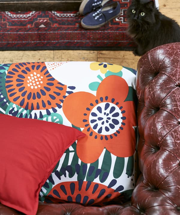 A close-up of patterned fabric on the seat of a leather sofa and a black cat.