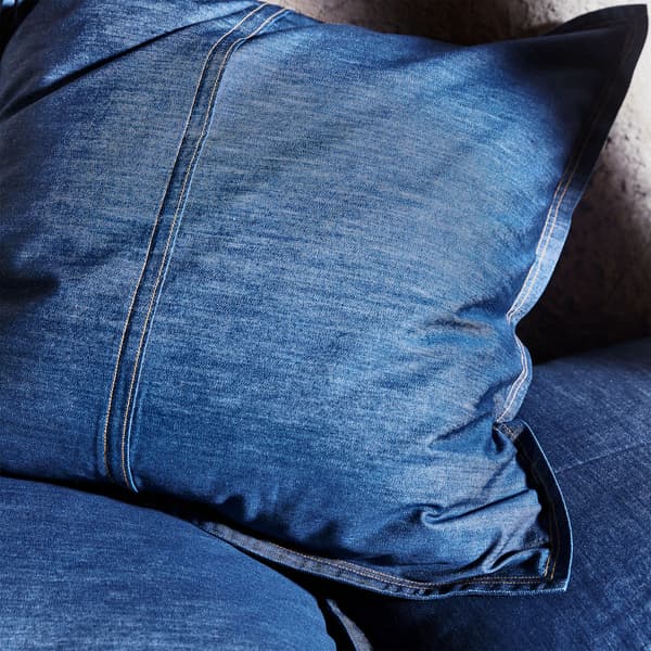 A close-up of SISSIL cushion cover shows its dyed blue denim with jean-inspired details such as brown-threaded seams.