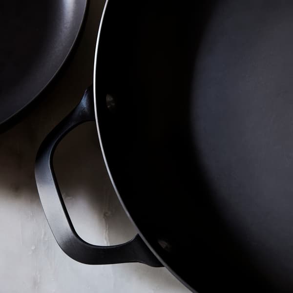 A close-up of the black carbon steel VARDAGEN frying pan with a handle placed on a grey marble countertop.