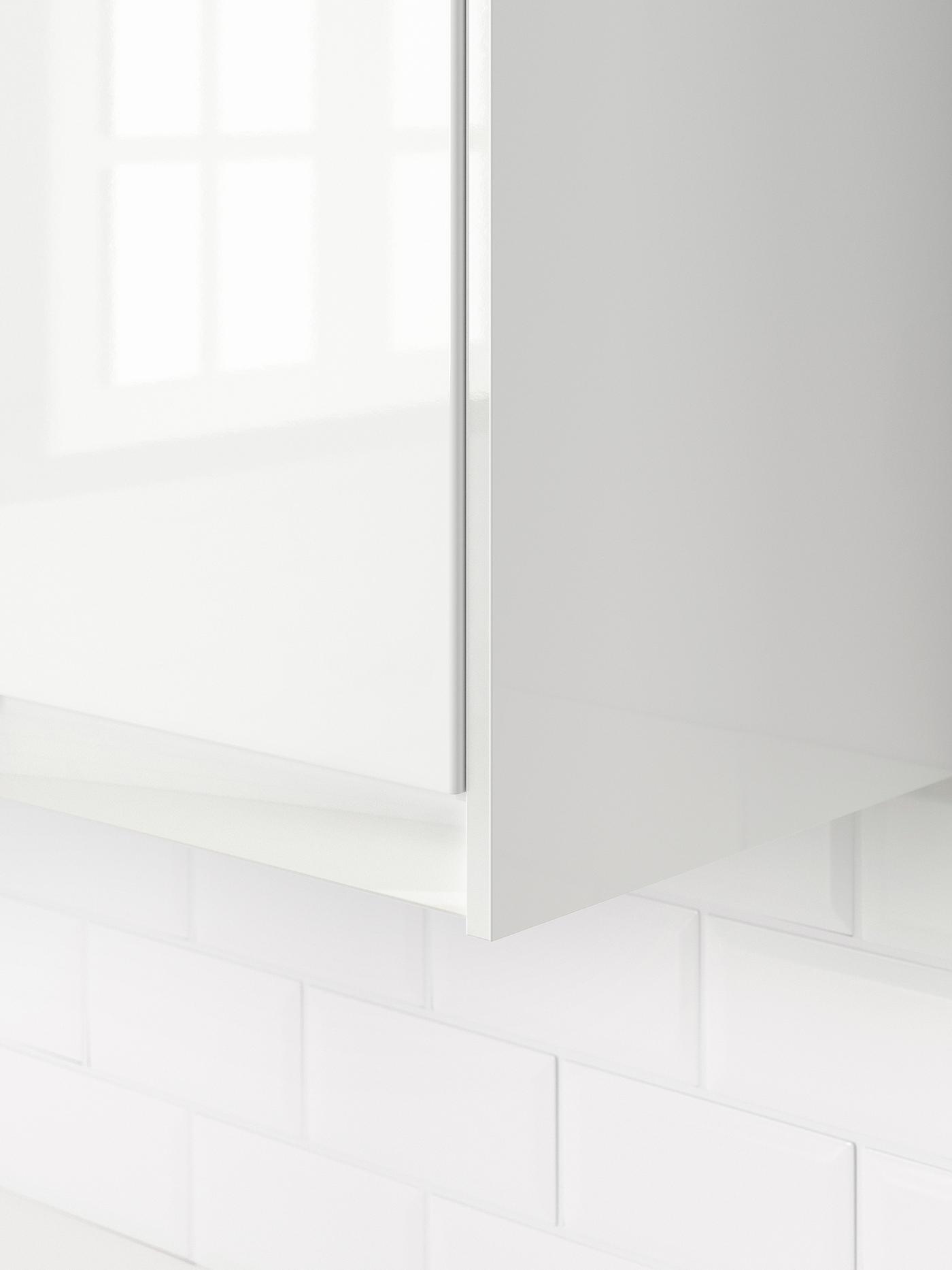 A close-up of the bottom corner of a white wall-mounted cabinet with a white high-gloss door.