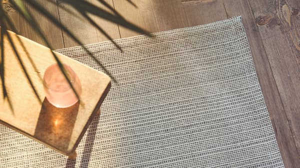 A close-up of the flatwoven TIPHEDE rug with a side table placed on it, while sunlight streams in on one side.