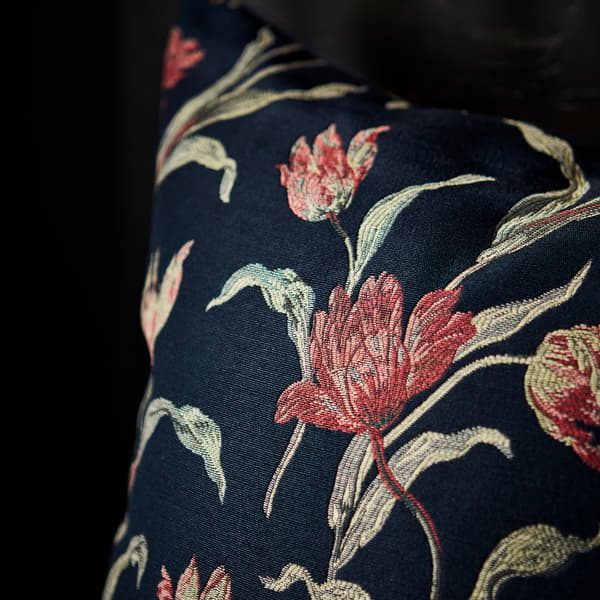 A close-up of the hand-embroidered ÅLANDSROT cushion with a jacquard-woven tulip pattern against a dark-blue background.