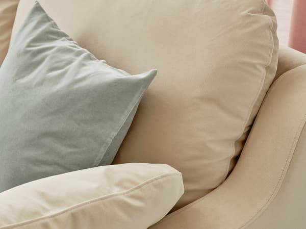 A close-up of the high-backed VINLIDEN sofa in beige with generous dimensions propped with a light blue cushion.