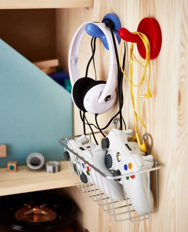 A close-up of the inside of a cabinet door with hooks holding headphones and a metal basket holding game controllers.