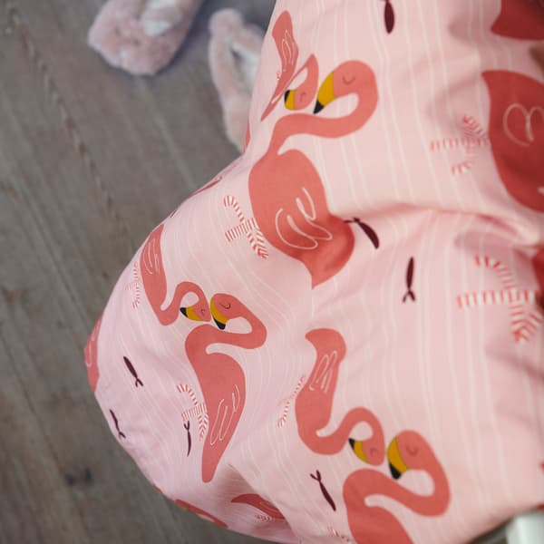 A close-up of the pink RÖRANDE quilt cover with a print of cuddling flamingos set against a wooden floor background.