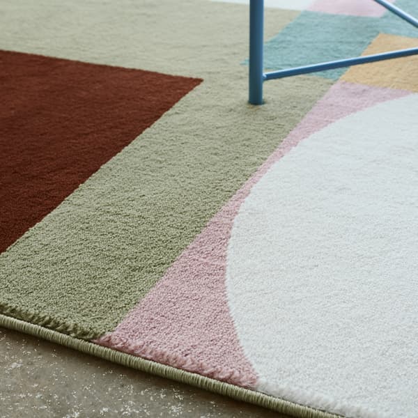 A close-up of the soft low pile of STENMÄTARE rug with a Bauhaus pattern in tones of pink, mint, blue, yellow and dark red.