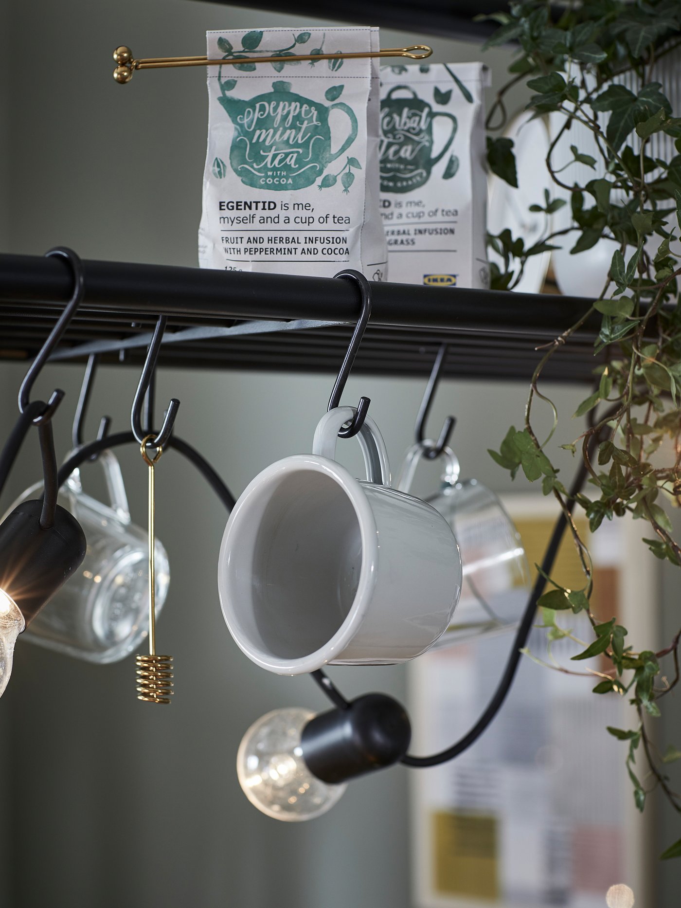 A close-up of the top rack shelf of an island used for hanging cups and a honey dipper on hooks and for storing tea.