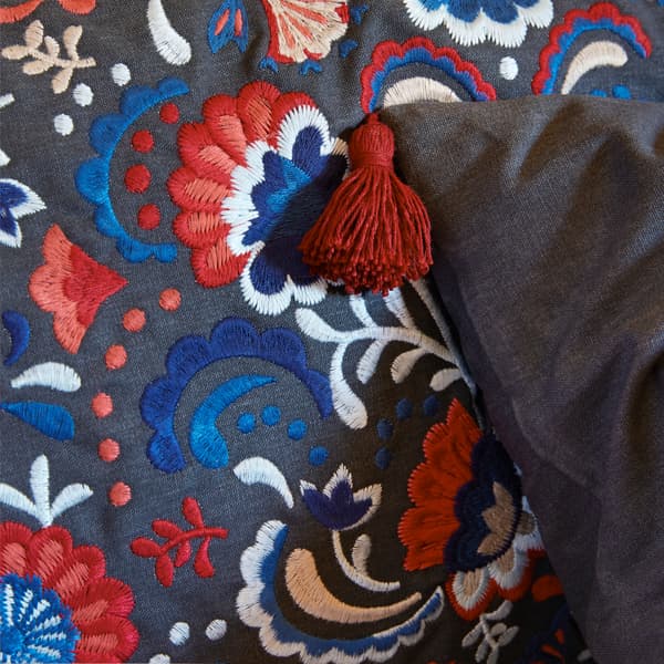 A close-up of the traditional-styled floral embroidery of SKOGSKORN cushion with tassels in the corners.