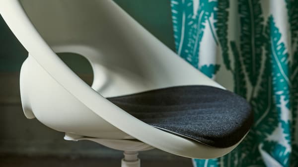 A close-up of the white LOBERGET/BLYSKÄR swivel chair with a rounded retro design placed in a green room.