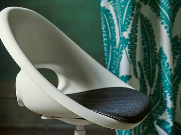 A close-up of the white LOBERGET/BLYSKÄR swivel chair with a rounded retro design placed in a green room.