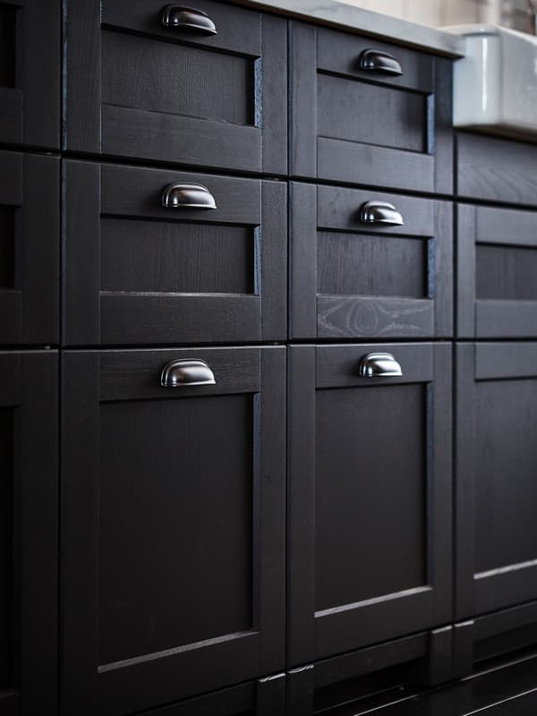A close-up of traditional stained black LERHYTTAN drawer fronts with black ENERYDA cup handles in a kitchen setting.
