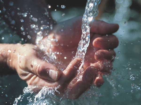 A close-up of two hands being held out and open with water pouring into them.