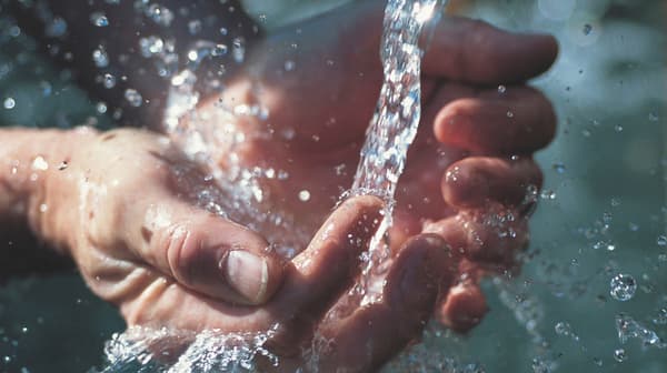 A close-up of two hands being held out and open with water pouring into them.