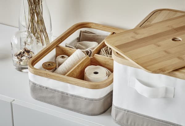 A close-up of white and grey IKEA storage boxes with wooden lids and sewing items stored in wooden compartments inside.