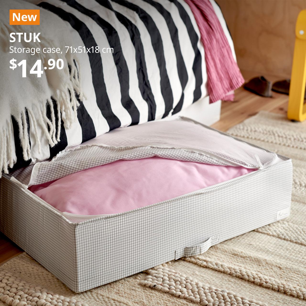 A close-up shot of a half unzipped white/black STUK storage case with a pink bedsheet set kept. An orange "NEW" label is on the top left of the image with black text that reads: STUK, Storage case, 71x51x18 cm, $14.90.