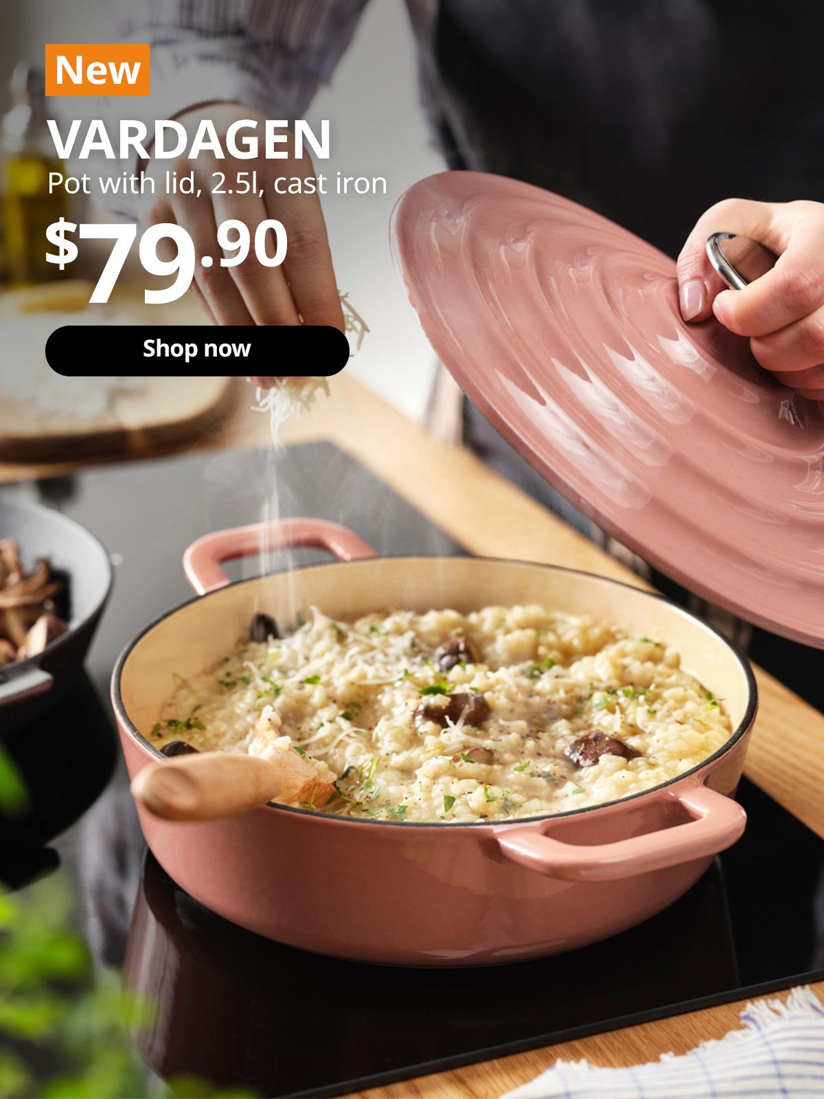 A close-up shot of a light pink VARDAGEN cast iron pot with lid being use to cook risotto on a induction stove top in a kitchen setting. A orange tag with white text that reads 'New', followed by white text overlaying image that reads 'VARDAGEN, Pot with lid, 2.5l, cast iron, $79.90'.
