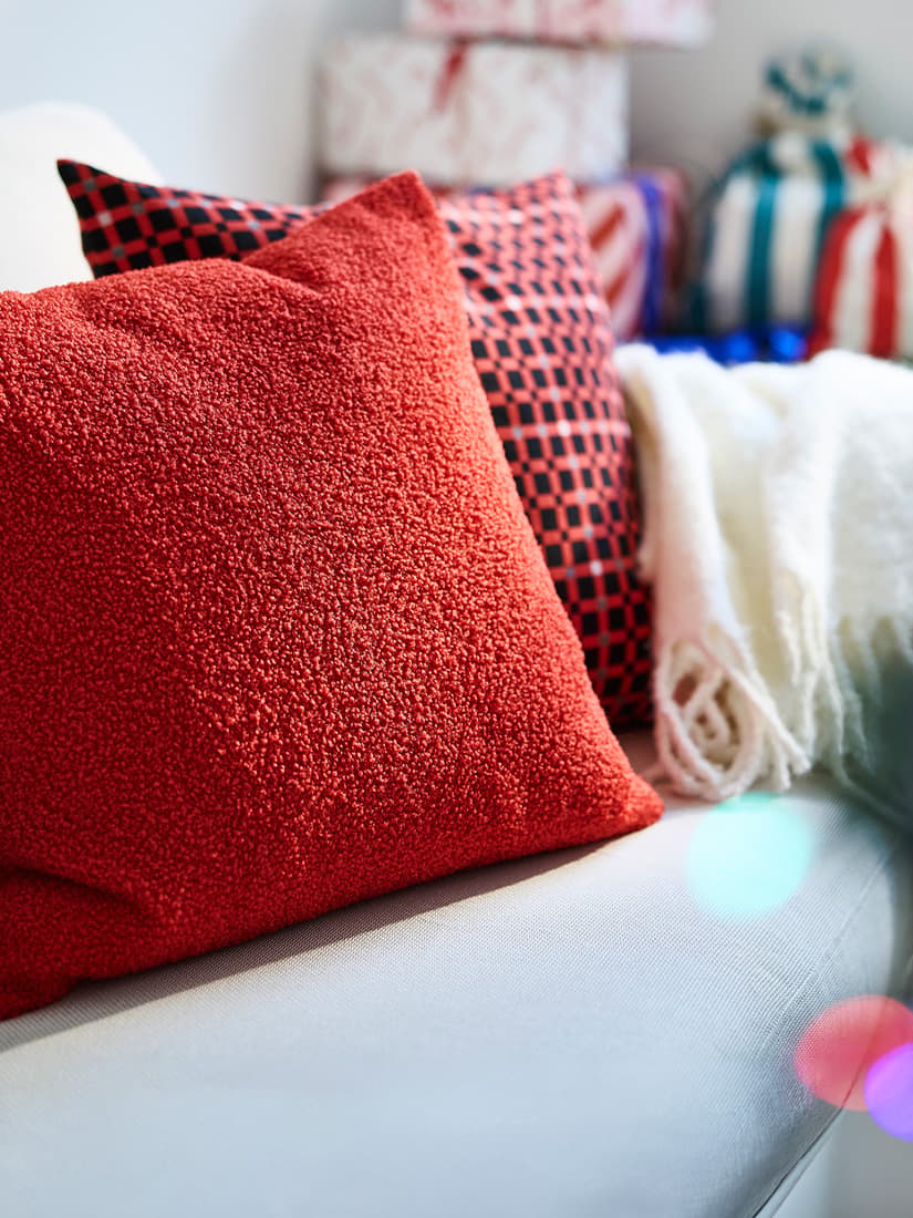 A close-up shot of a red VINTERFINT 2026 cushion in red placed next to a red checkered patterned VINTERFINT 2026 cushion on a light grey sofa in a living room setting.