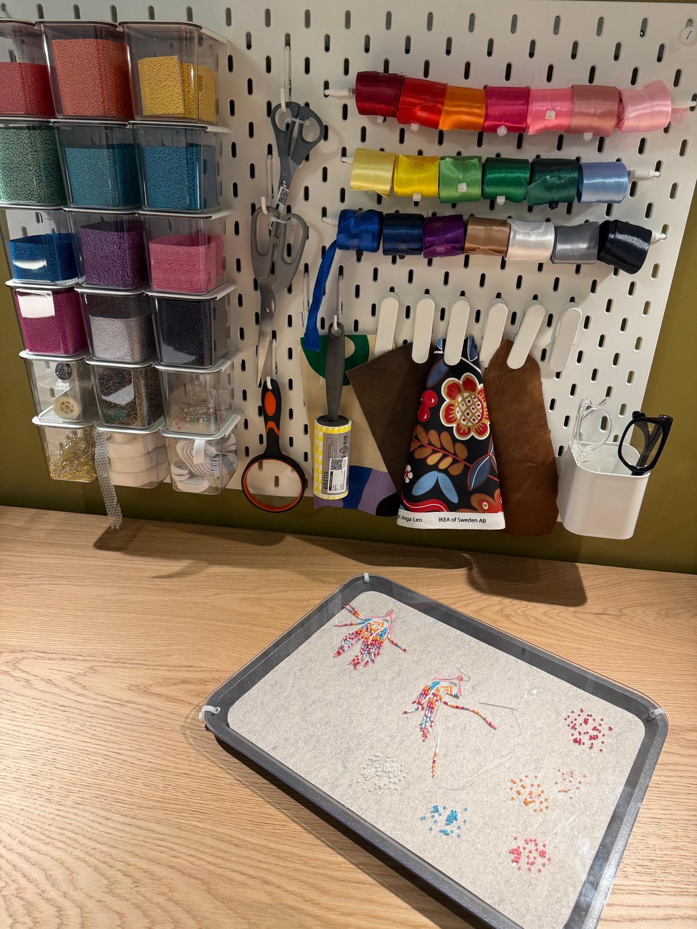 A close up shot of a white SKADIS pegboard holding colorful crafting accessories.
