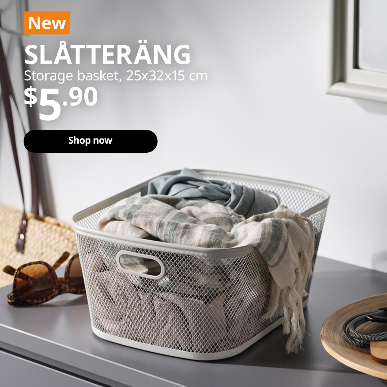 A close-up shot of a white SLATTERANG storage basket with a scarfs placed in it on top of a grey chest of drawer. A orange tag with white text that reads 'New', followed by white text overlaying image that reads 'SLÅTTERÄNG, Storage basket, 25x32x15 cm, $5.90'.
