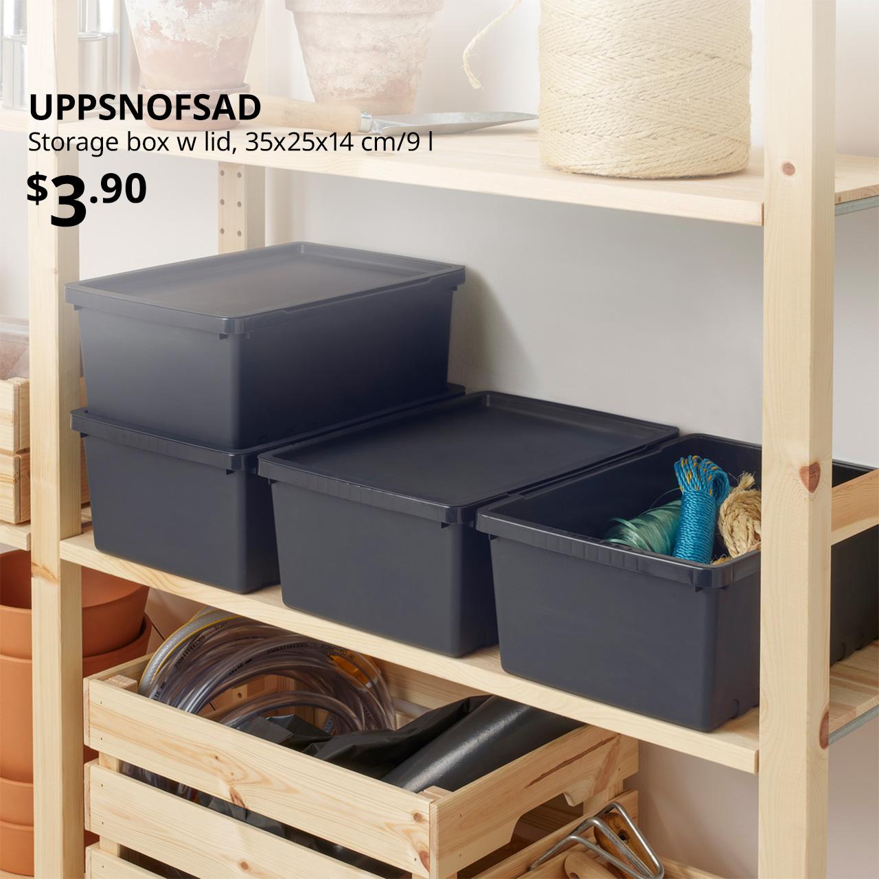 A close-up shot of several black UPPSNOFSAD storage boxes with lids being used as small storage & organisation and placed on a pine IVAR shelving unit. On the top left corner, black text overlay image that reads 'UPPSNOFSAD, Storage box w lid, 35x25x14 cm/9 l, $3.90'.