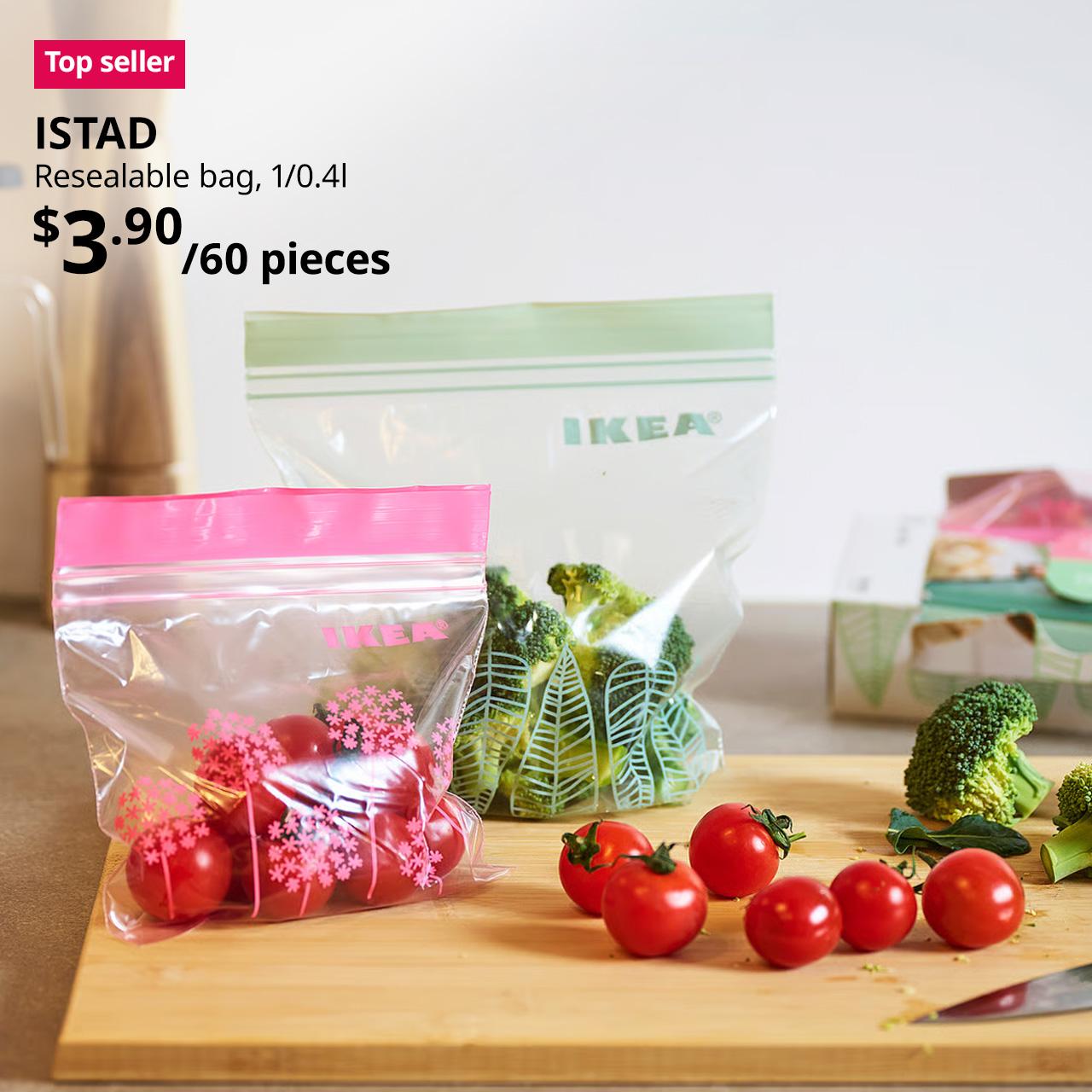A close-up shot of the kitchen counter, showcasing the ISTAD resealable bag in pink and green placed on the bamboo APTITLIG chopping board with cherry tomatoes and broccoli. On the top left corner, a red/pink tag with white text that reads 'Top seller', followed by black text overlaying image that reads 'ISTAD, Resealable bag, 1/0.4l, $3.90/60 pieces'.