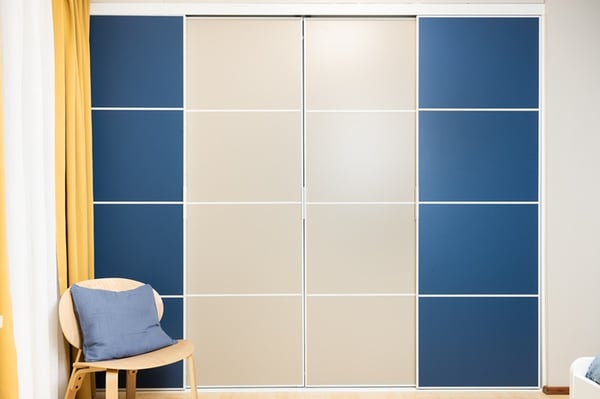 A closed wardrobe with sliding doors in blue and beige panels, creating a clean and organized look in an attic room.