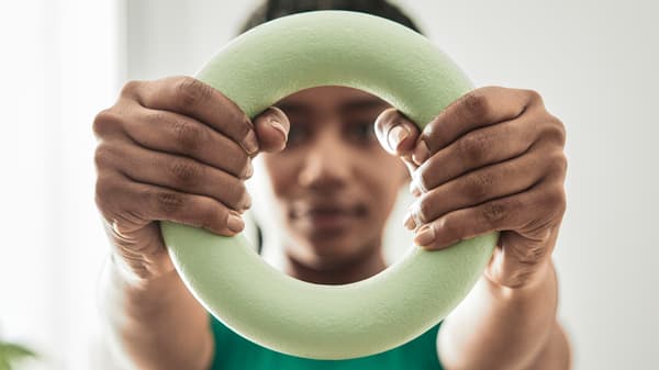 A closeup image of a girl wearing a green workout top, holding a round DAJLIEN training weight in front of her.