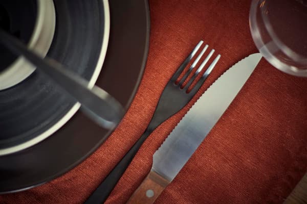 A closeup of a black matt fork and steak knife, next to black plates.