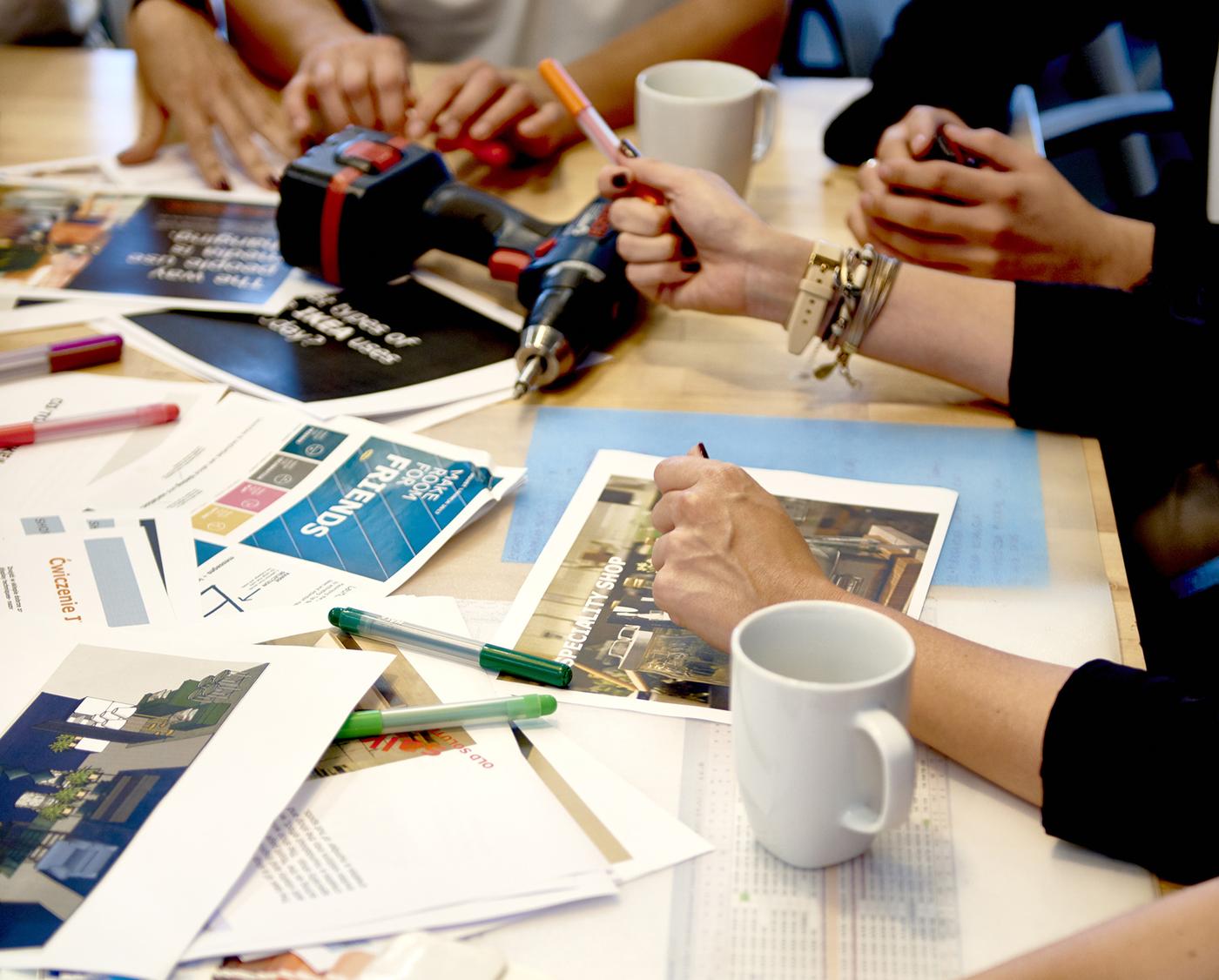 A closeup of a desk in an IKEA office with lots of documents and co-workers discussing a project.