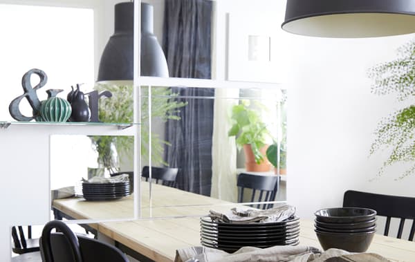 A closeup of a dining room wall decorated with several rectangular and square mirrors above a pine dining table.