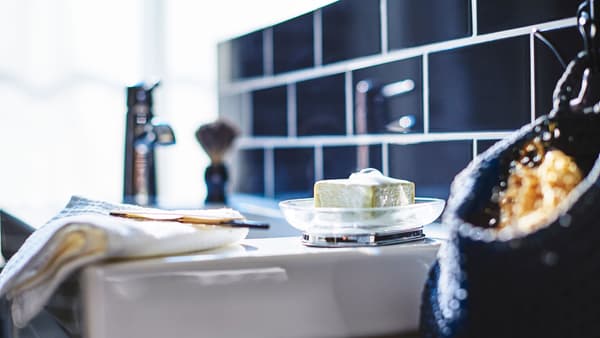 A closeup of a white sink, featuring a soap in a bowl and a razor on a towel.